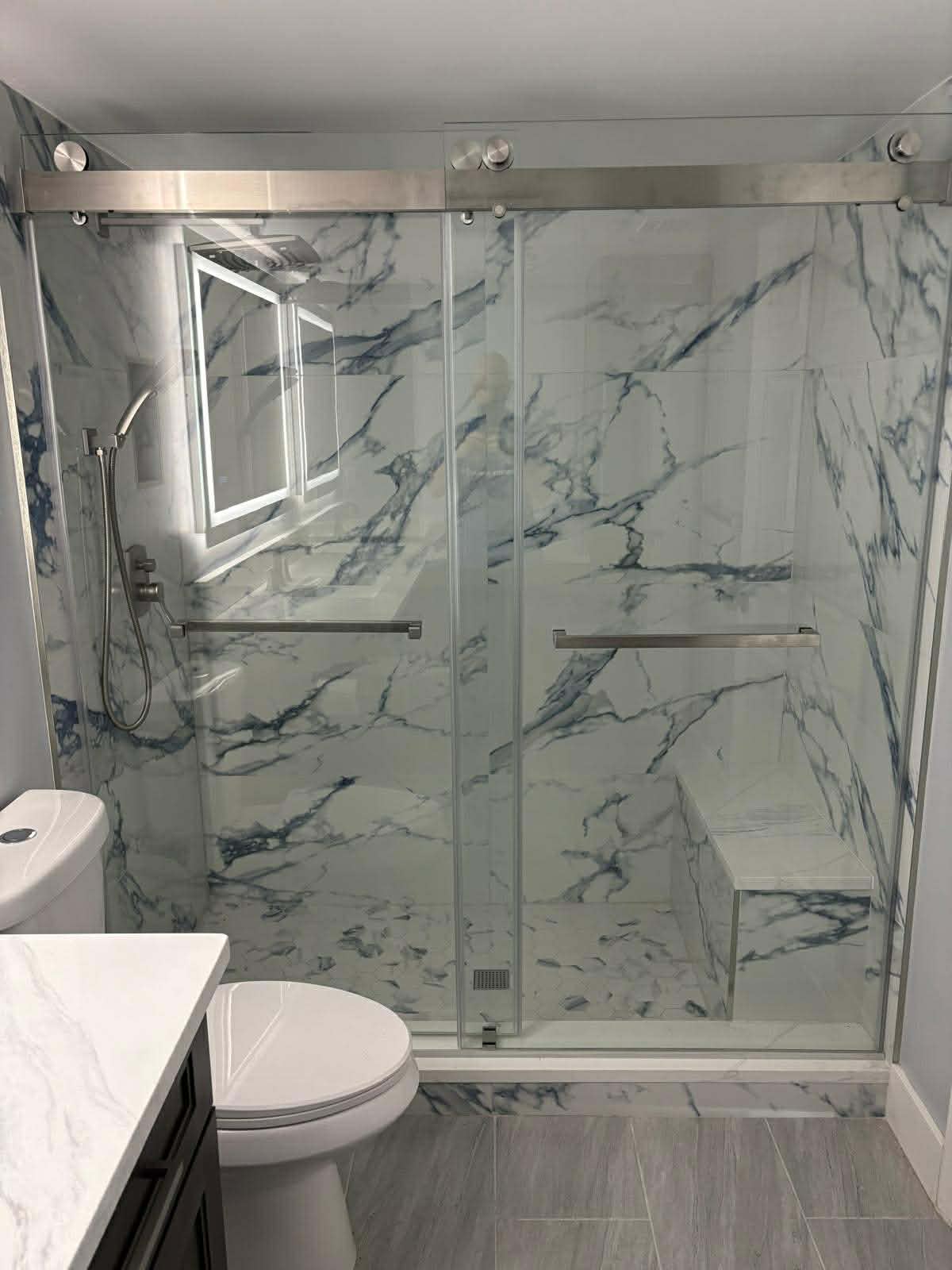 Completed luxury bathroom remodel featuring frameless glass shower enclosure and marble tile by Custom Bath and Tile
